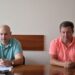 Двоє чоловіків у світлих футболках-поло сидять за столом під час робочої наради в адміністративному приміщенні.