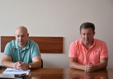 Двоє чоловіків у світлих футболках-поло сидять за столом під час робочої наради в адміністративному приміщенні.