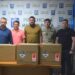 П'ятеро чоловіків стоять за столом у приміщенні Рівненської міської ради. На столі розміщено три великі коробки з обладнанням Starlink.