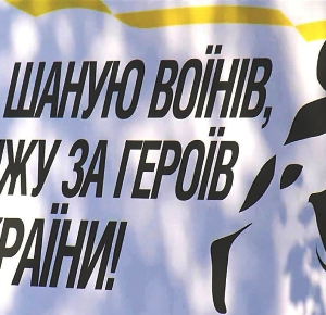 Банер із патріотичним написом великими чорними літерами: «Шаную воїнів, біжу за Героїв України!».