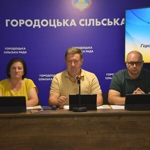 Сільський голова Сергій Поліщук та представники Городоцької сільської ради під час проведення 65-ї позачергової сесії. На задньому плані — символіка громади та екран із назвою пленарного засідання.