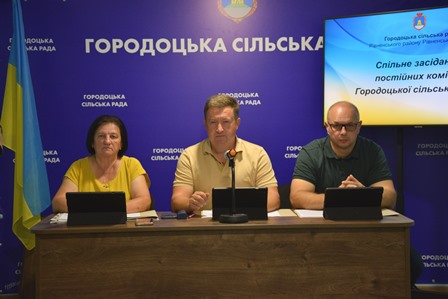 Сільський голова Сергій Поліщук та представники Городоцької сільської ради під час проведення 65-ї позачергової сесії. На задньому плані — символіка громади та екран із назвою пленарного засідання.