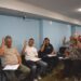 У залі засідань кілька учасників піднімають руки під час голосування. Люди сидять на стільцях із документами в руках.