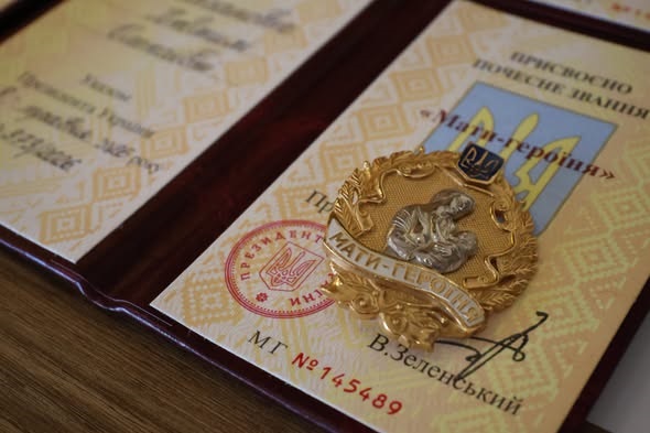 Посвідчення до почесного звання «Мати-героїня» та нагрудний знак «Мати-героїня», розміщені на столі.