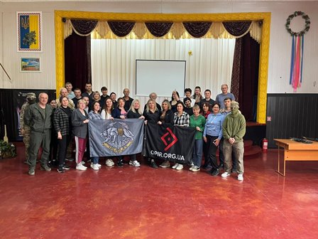 Групове фото учасників навчання у приміщенні Будинку культури. Люди стоять разом перед екраном, тримаючи прапори та символіку організацій.