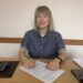 Жінка сидить за робочим столом в офісі та заповнює документи. На столі лежать папери, ручки та інші канцелярські речі.