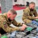 Двоє військовослужбовців у формі працюють у приміщенні, перебираючи та пакуючи дроти й кабелі.
