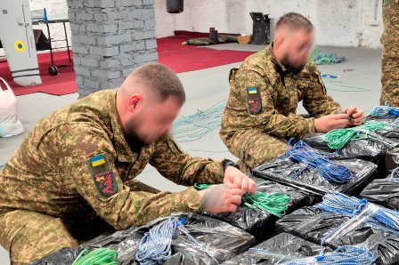 Двоє військовослужбовців у формі працюють у приміщенні, перебираючи та пакуючи дроти й кабелі.