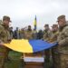 Військовослужбовці тримають Державний Прапор України над труною під час церемонії прощання із загиблим Захисником України на кладовищі.