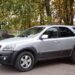 Сріблястий позашляховик Kia Sorento, переданий для потреб Захисника України, припаркований на подвір’ї біля огорожі та осінніх дерев.