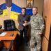 На фото — урочистий момент у робочому кабінеті. Двоє чоловіків стоять поруч і потискають один одному руки.